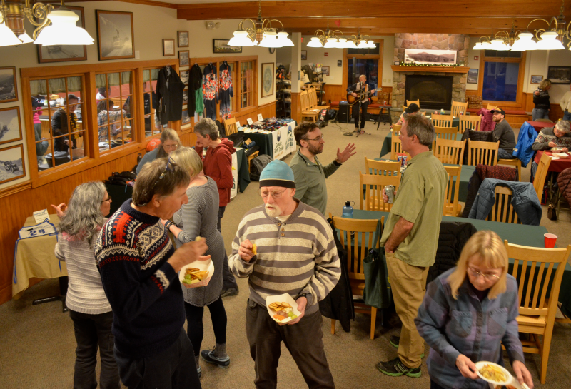 People socializing in a cozy room with tables, while a musician performs in the background.
