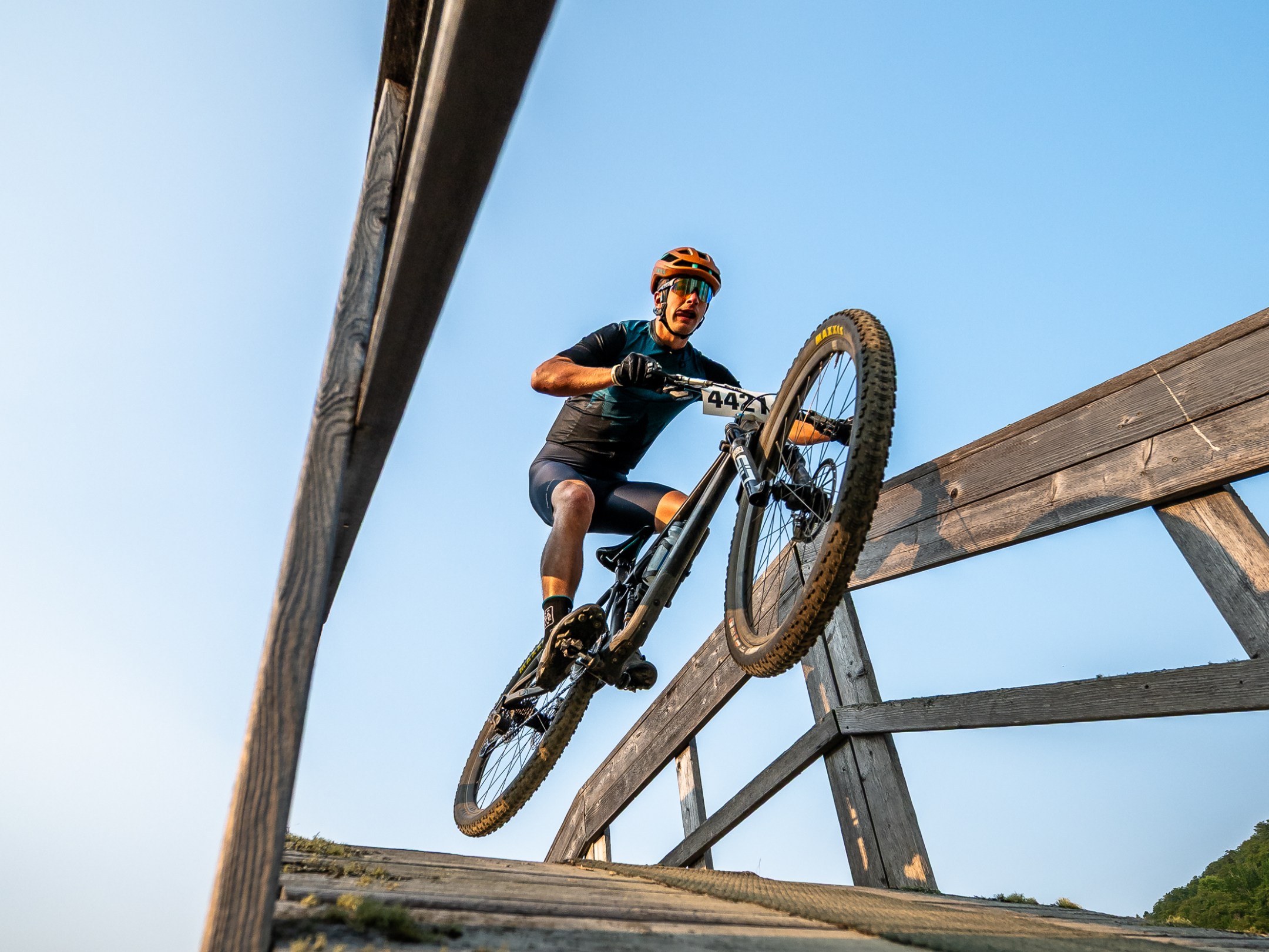 Mountain biker jumping over wooden bridge with blue sky background.