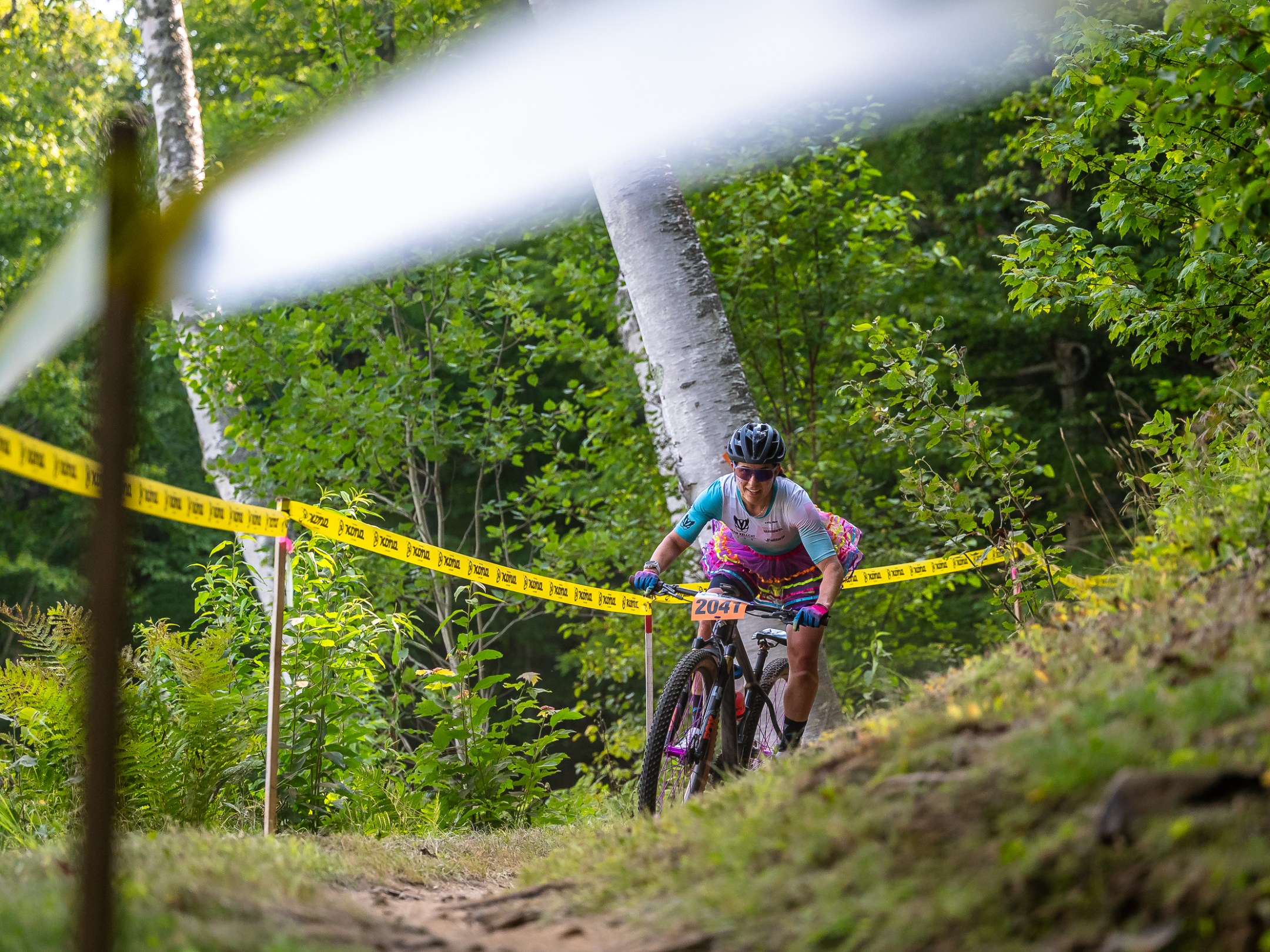 Cyclist on mountain bike race trail in forest with yellow barrier tape.
