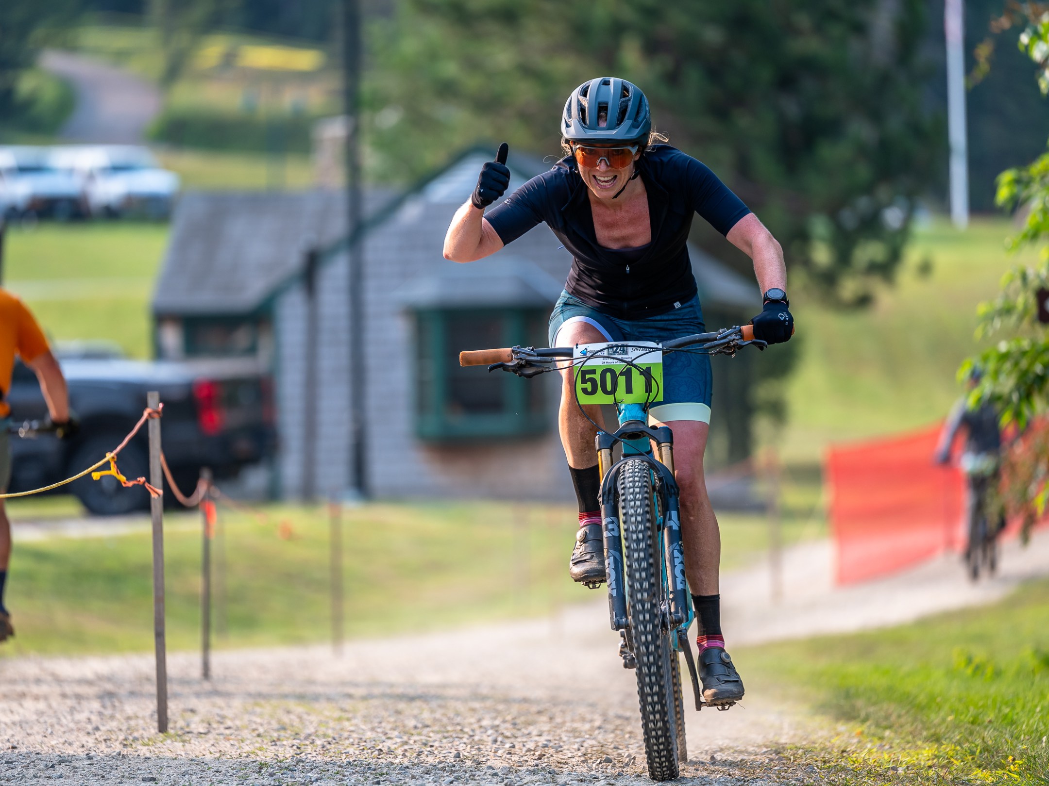 Cyclist giving thumbs up during race, wearing helmet and jersey.