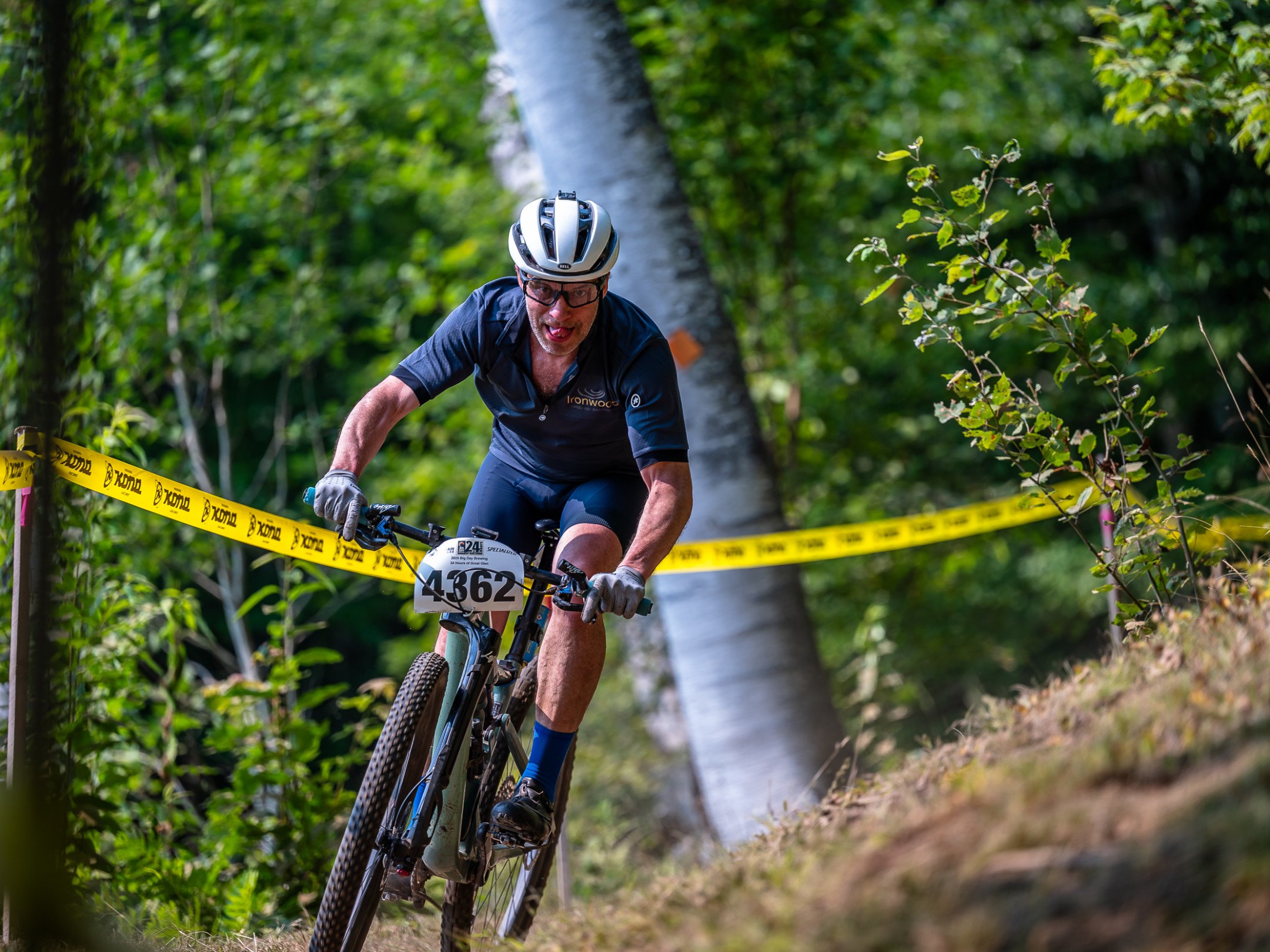 Cyclist number 4362 riding on a trail in a forest, surrounded by yellow tape.