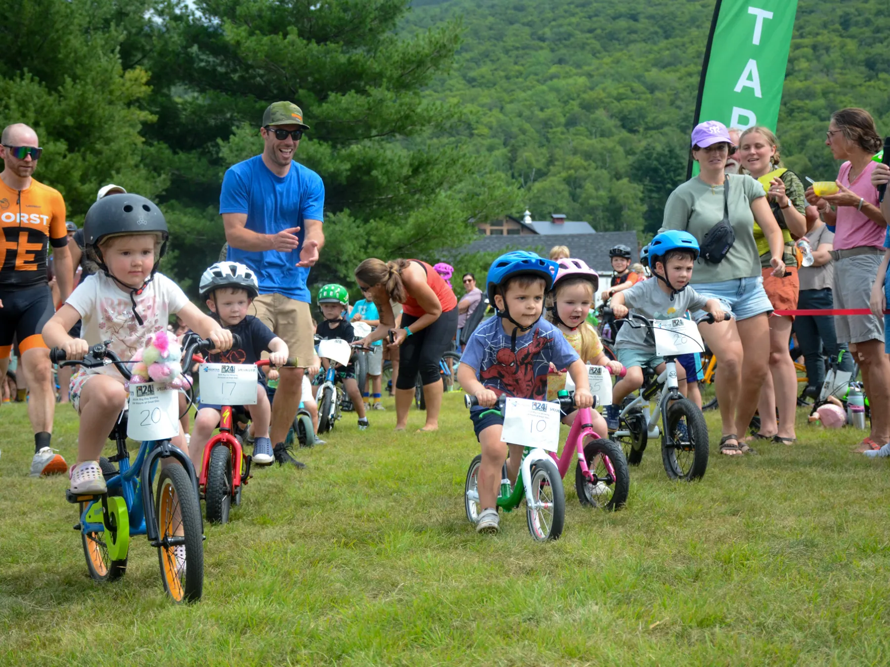 Children on bikes racing at an outdoor event with spectators.
