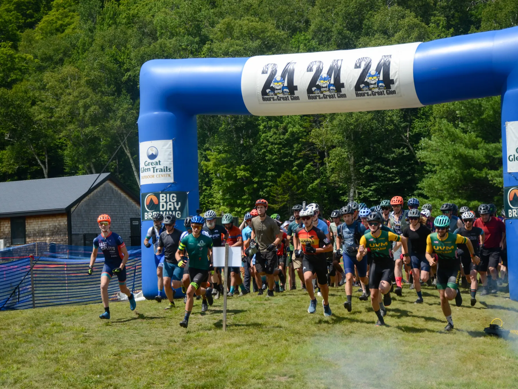 Cyclists start race under blue arch at outdoor event.